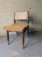 Front angle of one teak chair showing tapered legs with brass caps, worn original upholstery on seat and backrest.