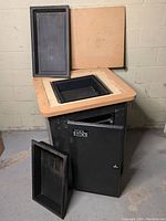 Full view of the multipurpose tool cabinet with router table top, flippable wooden cover beside it, open cabinet door showing storage area, and one black plastic tray positioned in the top recessed area and one tray beside the cabinet.