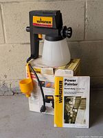 Wagner Power Painter with velocity test cup, original box, and instruction manual arranged together.