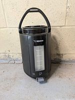 Photo of black Zojirushi thermal gravity pot dispenser showing front view with handle and water level gauge.