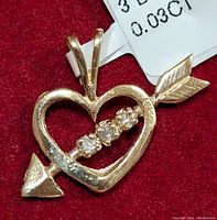 Close-up photo of the gold heart-shaped pendant with an arrow and three diamonds, showing detail and diamond sparkle.