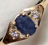 Close-up front angled view of oval blue sapphire and two round diamonds set in yellow gold ring.