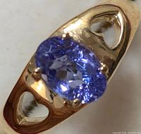 Close-up image of the ring showing the oval cut blue-purple tanzanite set in 10K yellow gold with heart cut-out band sides.