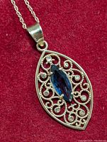 Front view of the pendant showing marquise blue sapphire center and filigree 14K gold design with diamond accents.