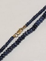 Close-up of sapphire rondelle beads and 14K yellow gold lobster clasp laid out on white background