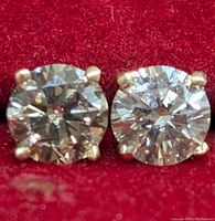 Close-up of two round brilliant cut brown diamonds in 4-prong gold settings on red velvet background.