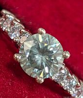 Close-up of round center moissanite in six-prong setting with side diamonds on band