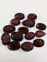 Multiple garnet gemstones in various faceted oval and rounded cuts shown on a white surface.