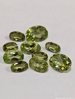 Ten genuine peridot loose gemstones displayed on a white background showing their oval faceted cut and olive green color.