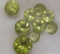 Close-up image of nine round cut peridot gemstones displaying light green color and faceted surfaces.