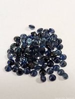Photo showing multiple loose blue sapphires in various sizes and shapes, primarily round, polished stones with faceted tops and smooth backs.