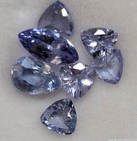 Close-up image of six faceted tanzanite gemstones in triangular and pear shapes, showing light to medium blue-violet color and internal clarity.
