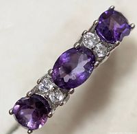 Top angle close-up of silver ring with three amethyst stones and clear accent stones.