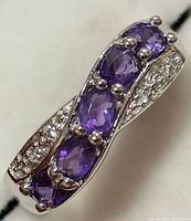 Close-up front angle of silver ring decorated with 5 oval amethyst and small white topaz stones in crossover setting.