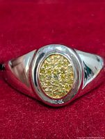 Close-up front view of silver ring with oval cluster of diamonds in gold-tone setting on red background.