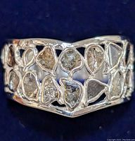 Close-up front view of the silver ring showing the cut-out leaf-shaped lattice design with raw diamond pieces in each section.