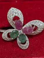 Close-up photo of the silver ring with emerald and ruby stones in a floral setting on a red background.