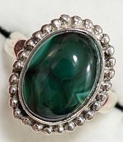Close-up of silver ring with polished oval Melakite gemstone surrounded by scalloped silver bezel setting.
