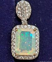 Close up of rectangular opal set in silver with cubic zirconia halo and decorated bale.