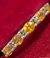 Close-up side view of the silver orange sapphire ring showing detail of the multiple oval orange sapphires in prong settings on the band.