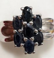Close-up front view of silver ring showing seven dark blue oval sapphire stones clustered and prong-set in silver.