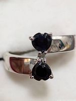 Close-up of silver ring with two heart-shaped deep blue sapphire stones and clear accent stones from above angle.