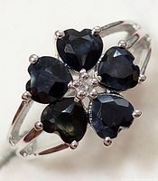 Close-up front view of silver ring with five heart-shaped sapphire stones and central cluster of white topaz stones.