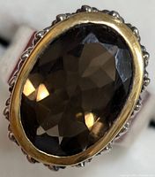 Close-up image of the oval faceted smokey quartz stone set in a silver ring with gold-tone bezel, showing front face details.