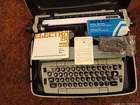 Smith Corona Electra 210 electric typewriter inside open case with manual, warranty card, and ribbon cartridge on top