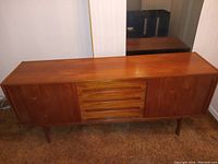 Full front view of teak credenza showing two cabinet doors and four central drawers on legs