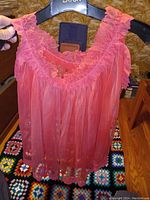 Front view of coral pink sheer baby doll lingerie held up on a hanger showing the lace ruffled neckline and flowing sheer fabric.