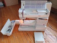 Pfaff sewing machine open on wooden floor, with removable storage tray of accessories laid to left and foot pedal to right