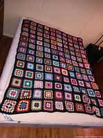 Photo of hand knit granny square blanket spread on bed showing colorful squares with black borders and overall condition.