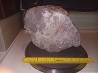Photo of a large light-colored mineral specimen rock on a black base with a yellow 12-inch ruler in front for size reference.