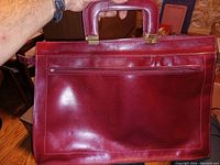 Reddish leather office purse front view showing zipper pocket and handle held by hand.