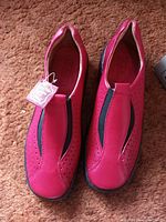 Top view showing the pinkish red leather upper with perforations and central elastic panel of the shoes, with attached tags.