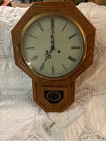 Front view of antique oak schoolhouse wall clock with octagonal frame, white face with Roman numerals, black hands, and brass bezel.
