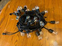 Coiled black wire string light with multiple clear LED filament bulbs, placed on wooden surface.