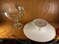 Photo showing the white ceramic cake plate and clear glass footed compote on a wooden shelf