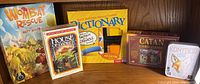 Photo of five boxed family games: Wombat Rescue, House of Danger, Pictionary Classic Edition, Kontour, Catan Card Game on a wooden surface.