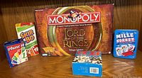 Photo showing Monopoly The Lord of the Rings Trilogy Edition game box, Skip-Bo, Phase 10, Mille Bornes, and Izzi puzzle box arranged on a surface