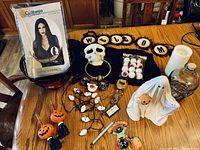 Overview of Halloween decorations including black wig in packaging, skull, treat bowl, battery-operated lights, candles, ghost figurine, pumpkin items, and a Halloween sign