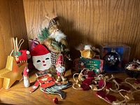 First photo showing wooden star ornament, fabric snowman, three Santa figures, nutcracker, blue boxed glass ornament, rustic bows, and small animal figurines.