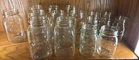 15 clear glass regular mouth mason jars arranged on wooden surface, showing various sizes and embossing including Ball, Kerr, and NW Electroglass.