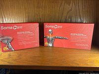 Two SomaCare heat pack boxes displayed side by side showing packaging with anatomical illustrations for knees and shoulder/neck.