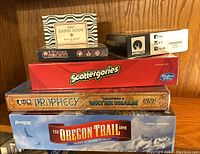 Stack of six tabletop family games including The Oregon Trail, Prophecy Expansion 2 Water Realm, Scattergories, Gloom Second Edition, The Games Room Movie Buff Quiz, and Koryo.