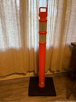 45 inch tall bright orange traffic delineator with two wide reflective white bands around the upper portion, supported by a square black weighted rubber base for stability. The top of the post has an integrated handle for easy transport.