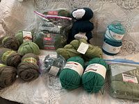 Photo showing multiple skeins of green yarn in various shades on a white lace background, including wool and silk blends.