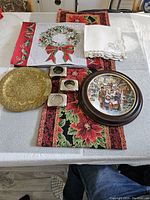 Overview of Christmas table linens with napkins, runner, place mats, tea light holders, decorative and framed plates on table