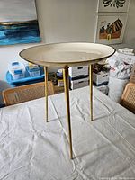Full view of the three-legged occasional table on a white cloth, showing round white surface with metallic gold legs.